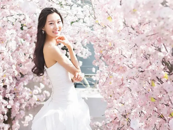 満開の桜の中で花嫁姿のキャリア女性が微笑む様子